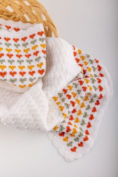 three crocheted baby blankets and a basket on a white surface with an orange, yellow, green, and red design