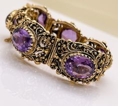 "GORGEOUS VINTAGE 14K AMETHYST  LINK BRACELET This bracelet is stunning!  Likely Circa 1940's but it could be older. 14K Yellow Gold Featuring 48.48 Carats of Faceted Oval Amethysts Push Clasp & Safety Chain Closures Marks: 14K and a Hallmark of the Goldsmith  Weight (g): 71.3 Clasp Style: Push Clasp, Safety Chain Carat Total Weight: 48.48 Stone Count: 6 Stone Shape: Faceted, Oval Color: Purple Saturation: Strong Type/Clarity: Eye Clean Transparency: Transparent Condition: Very Good Vintage Cond Heirloom Oval Bracelets For Formal Occasions, Antique Yellow Gold Collectible Bracelets, Antique Gemstone Bracelet For Anniversary, Victorian 14k Gold Bracelet With 17 Jewels, Antique Oval Hallmarked Bracelet, Vintage Formal Bracelet With Intricate Design, Formal Vintage Bracelet With Intricate Design, Vintage 14k Gold Bracelet With Intricate Design, Vintage Gold Bracelet With Intricate Design