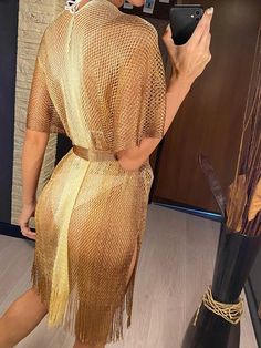 a woman taking a selfie in front of a mirror wearing a gold dress and black boots