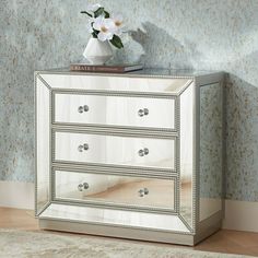 a white dresser with mirrored drawers and flowers on top