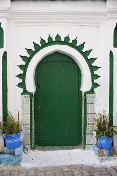 a green and white building with potted plants in front of the entrance to it