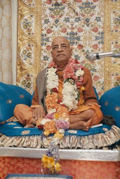 a man sitting on top of a blue couch in front of a wall covered with flowers