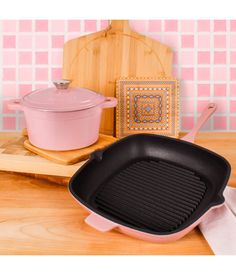 a pink cast iron skillet sitting on top of a wooden table next to a pot