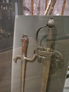 two old swords are on display in a glass case with a wooden stick sticking out of it