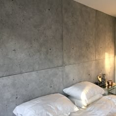 a bed with two white pillows on top of it next to a wall that is made out of concrete