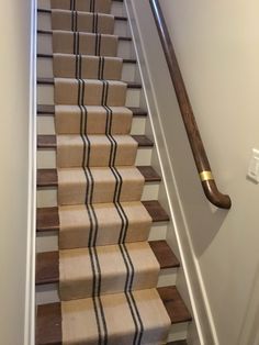 the stairs are lined with beige and black striped carpet, along with a wooden handrail