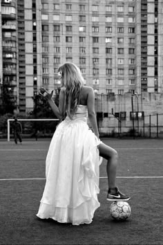 a woman in a white dress is sitting on a soccer ball and looking at her cell phone