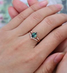 a woman's hand holding an engagement ring with a green stone in the middle