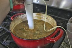 a red pot filled with soup sitting on top of a stove next to an electric blender