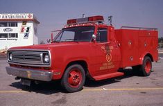 an old red fire truck is parked in a parking lot near a building with a sign on it