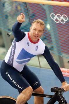 a man riding on top of a bike next to a flag and an olympic symbol