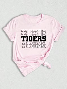 Introducing our Tigers Mascot Shirt, the perfect apparel for all the Tiger fans out there!  Whether you're a proud member of the Tigers team, a dedicated fan, or simply want to show your support, this shirt is a must-have addition to your collection. Designed with the iconic Tigers Mascot, this shirt captures the spirit and energy of your beloved team. Made with high-quality materials, this Tigers School Shirt is not only comfortable but durable as well. You'll love the softness of the fabric ag Band Merch T-shirt With Letter Print And Crew Neck, Cotton Slogan T-shirt For Fan Gear, School Spirit Short Sleeve T-shirt With Letter Print, School Spirit Graphic T-shirt Fan Gear, School Spirit Graphic T-shirt For Fan Gear, School Spirit Graphic Print T-shirt For Fan Gear, School Spirit Graphic T-shirt, Fan Apparel T-shirt With Letter Print, Pink Crew Neck T-shirt For Sports Events