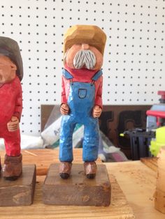 two wooden statues of men with hats and overalls on top of wood planks