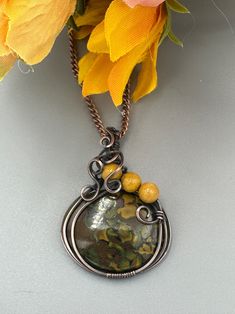 a close up of a necklace on a table with flowers in the background and an orange flower