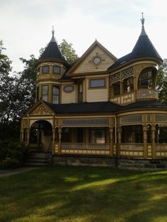 an old victorian style house in the middle of a field with trees and grass around it