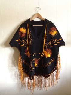 "Mexican folk embroidered poncho / cape / serape. Stunning. Deep black wool with vivid gold and copper embroidery. Collar with gold fabric beneath. Detailed embroidery on front and back. Beautiful hem fringe and long, gold cord at neck The condition is clean and rustic. No holes, wear or split seams. There are a few, expected pulls in the vintage embroidery hand work. Approximate Measurements: No tags. Underarm to underarm-29\" Sleeve length- 15\" - Short sleeve measured from hem of sleeve to ed Embroidered Long Sleeve Poncho For Festival, Black Shawl Cape For Festival, Black Bohemian Cape For Festivals, Bohemian Black Cape For Festival, Traditional Embroidered Poncho For Winter, Bohemian Black Poncho For Fall, Traditional Embroidered Winter Poncho, Traditional Black Cape For Fall, Winter Embroidered Long Sleeve Poncho