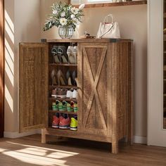 a wooden cabinet with several pairs of shoes in it and a vase full of flowers