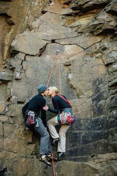 two people climbing up the side of a rock face each other with ropes attached to their backs