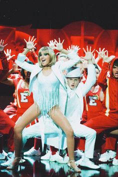 a group of people on stage with their hands in the air and wearing white outfits