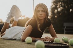 a woman laying on the ground with tennis balls and racket in front of her