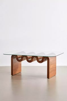 a glass and wood coffee table with wavy curves on the top, in front of a white wall