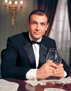 a man in a tuxedo sitting at a table with a wine glass on it