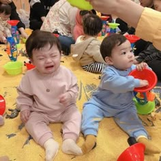 two babies sitting on the floor with their mouths open and hands holding plastic cups in front of them