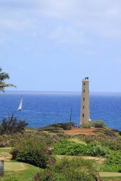 a light house sitting on top of a lush green hillside next to the ocean with sailboats in the distance