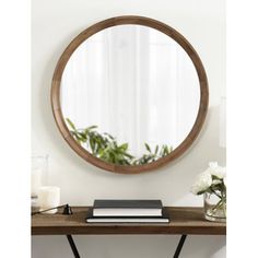 a round mirror sitting on top of a wooden table next to a vase with flowers