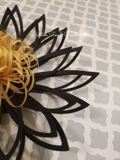 a flower made out of black and yellow paper on top of a white tablecloth