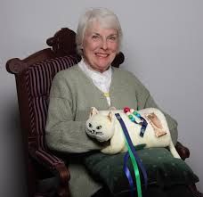 an older woman sitting in a chair holding a stuffed cat on top of a pillow