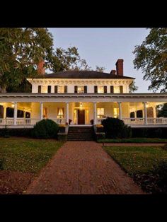 a large white house sitting on top of a lush green field next to tall trees