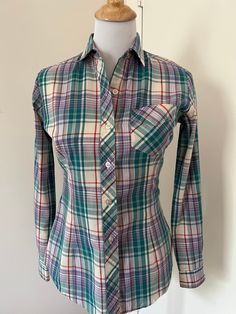 Cute 80s style madras plaid button up shirt from Mervyn's Hot Line. Made of a lightweight cotton blend. Spread collar  Patch pocket on breast. Long tail. Barrel cuffs. Yoked back. Fitted cut with darts in front and back. Probably late 70s / early 80s.  In very good used condition.  Tagged Mervyns Hot Line Size 9  55/45 cotton poly  Measurements taken flat buttoned Pit to pit 18" Waist: 16" Hips: 17" Sleeve: 30"  Length shoulder seam to hem: 26" Mervyns of California  Preppy style Madras plaid Fitted shirt  Long sleeve plaid shirt  80s style Plaid Top With Spread Collar And Button Closure, Plaid Top With Button Closure And Spread Collar, Fall Cotton Fitted Shirt, Fitted Cotton Shirt For Fall, Cotton Top With Spread Collar For Fall, Plaid Shirt With Spread Collar And Buttons, Long Sleeve Cotton Flannel Shirt, Fitted Plaid Cotton Shirt, Classic Multicolor Shirt For Fall