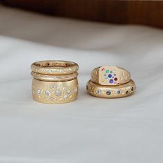 three gold rings sitting on top of a white bed next to each other with different colored stones