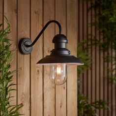 an outdoor light on the side of a wooden wall next to a potted plant