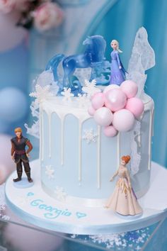 a frozen princess themed cake with figurines on top and balloons in the air