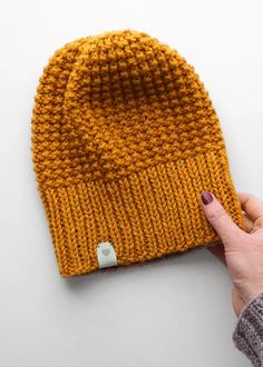 a hand is holding up a yellow knitted beanie on a white surface,