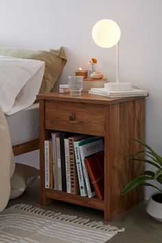 a nightstand with books on it next to a bed and a potted plant in the corner