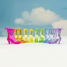 a row of colorful rain boots sitting on top of a snow covered ground with clouds in the background