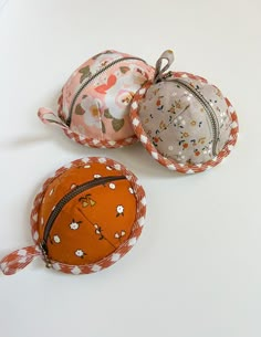 three small purses are sitting on a white surface, one is orange and the other is pink