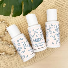 three bottles of hand sanitizer sitting on top of a straw hat next to a plant