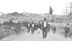 black and white photograph of men walking down a dirt road with flags in the foreground