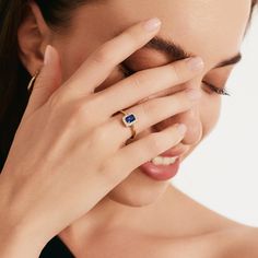 a woman holding her hand up to her face while wearing a ring with a blue stone on it