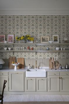 a white kitchen sink sitting under a window next to a counter top with flowers on it