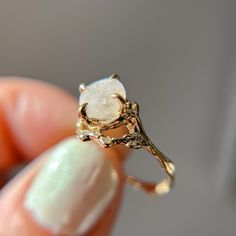 a close up of a person's hand holding a gold ring with a white stone