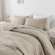 a bed covered in a beige quilt and pillows