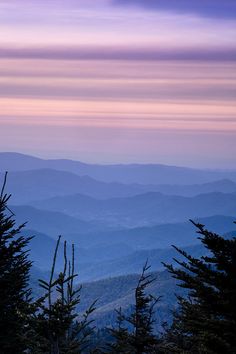 the mountains are covered in purple and pink hues as the sun sets over them