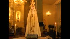 a statue of the virgin mary in front of a church with candles and chandeliers