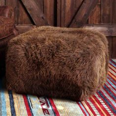 a brown sheepskin bean bag sitting on top of a striped rug next to a leather chair