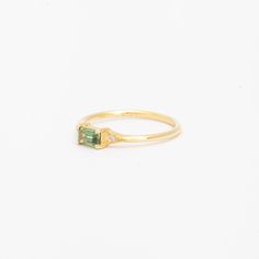 a yellow gold ring with an emerald and diamond set in the middle, on a white background